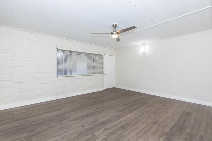 Bright and airy living room featuring sleek wood flooring, modern ceiling fan, and large window with blinds for natural light.