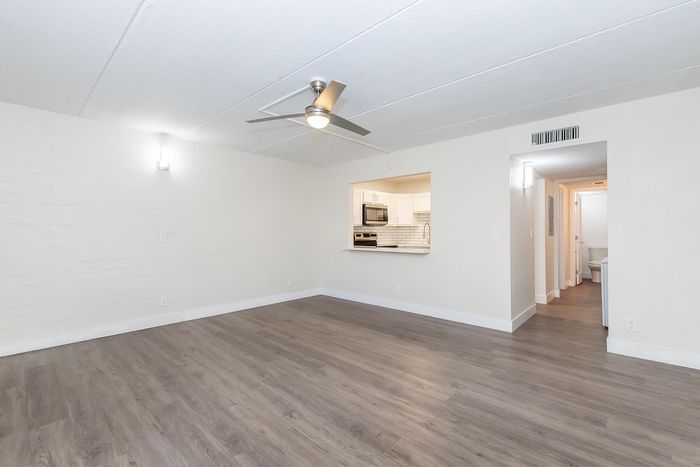 Modern living room with sleek hardwood floors, energy-efficient ceiling fan, and a peek-a-boo view into a contemporary kitchen.