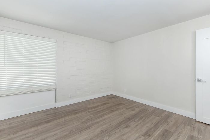 Modern empty room with sleek wooden flooring and a bright window featuring stylish blinds, perfect for personalization.
