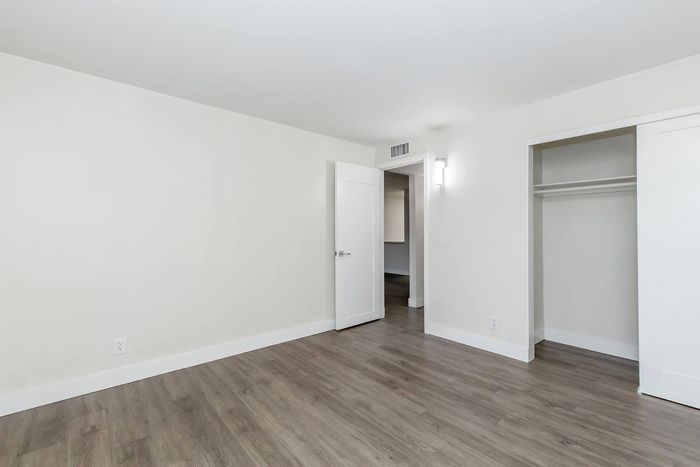 Bright, modern bedroom with elegant hardwood floors, spacious closet, and freshly painted white walls.