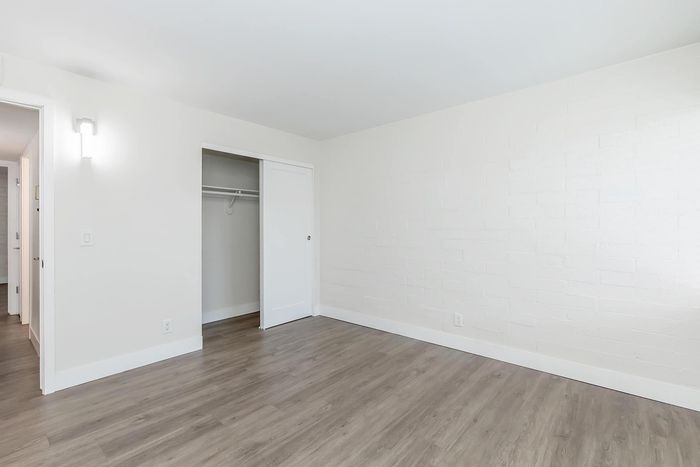 Bright and spacious bedroom with sleek laminate flooring, modern white walls, and a convenient built-in closet.
