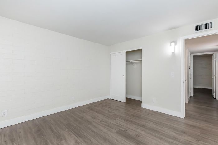 Bright, modern bedroom with sleek hardwood floors, open closet space, and contemporary lighting.
