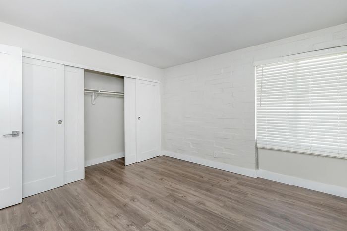 Chic and modern bedroom with elegant wood flooring, ample closet space, and bright natural light from wide windows featuring sleek blinds.