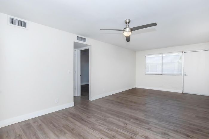 Bright and modern living area with sleek hardwood floors, large window, and stylish ceiling fan, offering a warm and inviting ambiance.