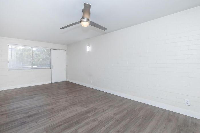 Bright, airy room with sleek hardwood floors, modern ceiling fan, and large window for abundant natural light.