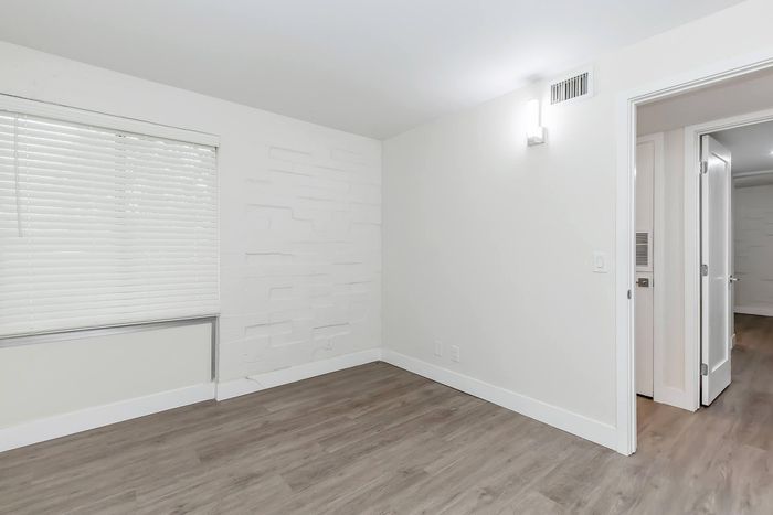 Bright and inviting room with modern white walls and sleek wooden flooring, featuring ample natural light from large windows.