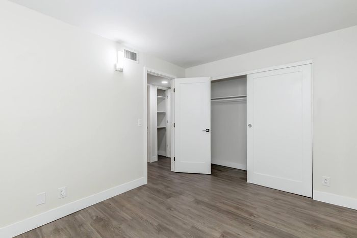 Bright and spacious bedroom with sleek wood flooring, ample closet space, and modern white doors.