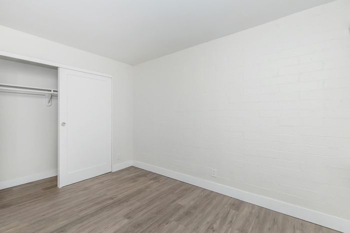 Bright and airy room with sleek hardwood floors, pristine white walls, and a modern sliding door closet, perfect for a cozy bedroom setup.