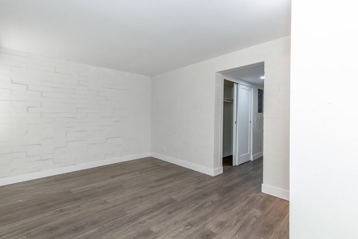 Modern apartment room with sleek hardwood flooring and textured white brick walls, featuring an open walk-in closet with sliding doors.