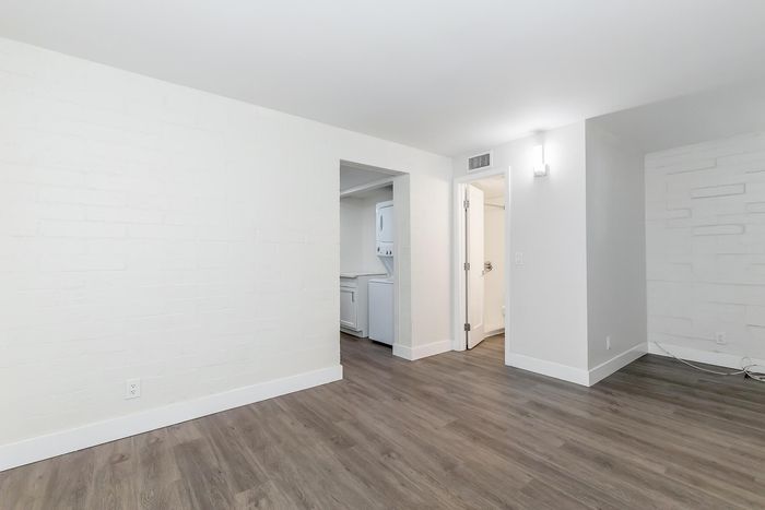 Modern apartment space with sleek hardwood floors, neutral white brick walls, and convenient in-unit laundry.