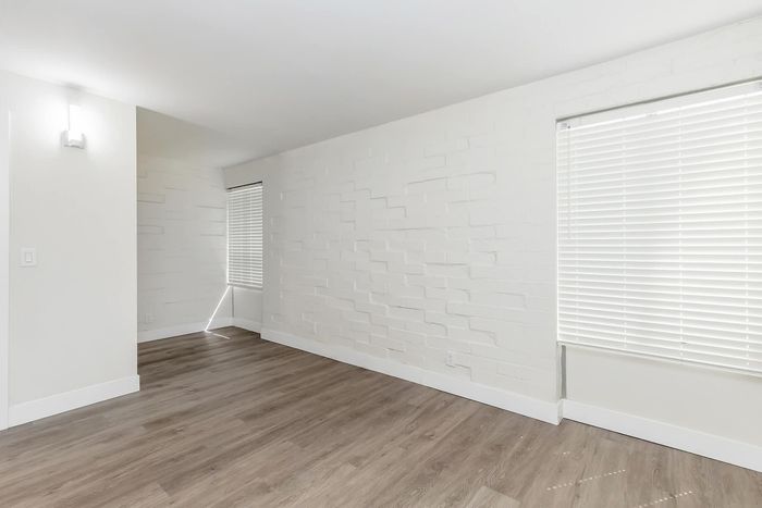 Modern apartment interior with fresh white walls, textured design, large windows with blinds, and elegant wood flooring.