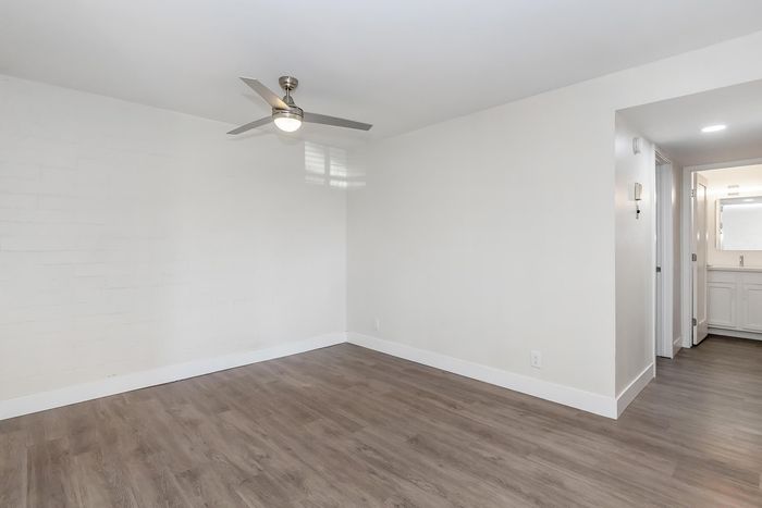 Elegant living room with sleek ceiling fan and modern hardwood floors leading into a bright hallway.