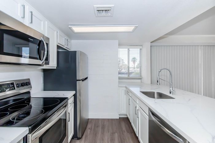 Modern kitchen with sleek stainless steel appliances, pristine white cabinetry, and elegant marble countertops, featuring ample natural light from large windows.