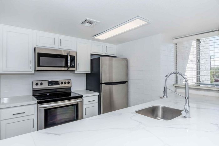 Modern kitchen with stainless steel appliances, sleek white cabinetry, and a stylish marble countertop, bathed in natural light.