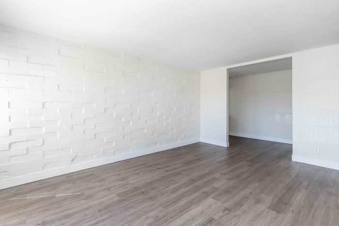 Bright and airy living space with modern wood flooring and stylish white brick accent wall, perfect for a contemporary lifestyle.