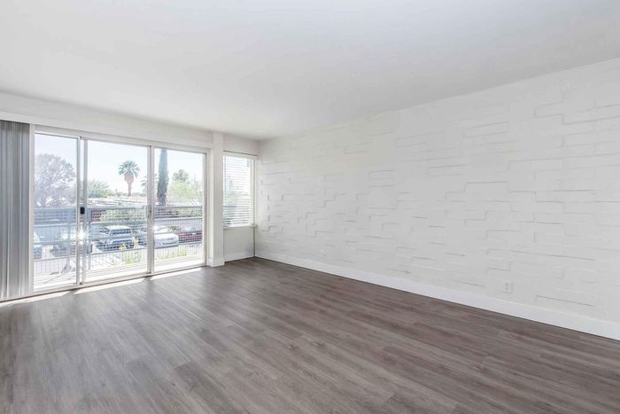 Bright and spacious living area with modern wood flooring, large windows, and chic textured walls, ideal for stylish living.