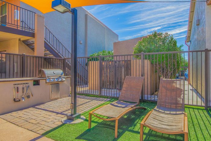 Inviting outdoor space with modern grill, two sun loungers, and vibrant greenery, perfect for relaxation and entertaining.