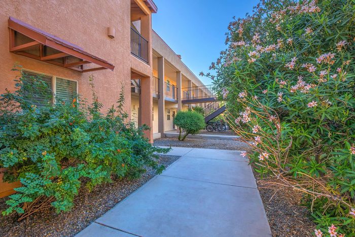 Charming apartment exterior with lush greenery, colorful flowers, and modern architecture on a sunny day.