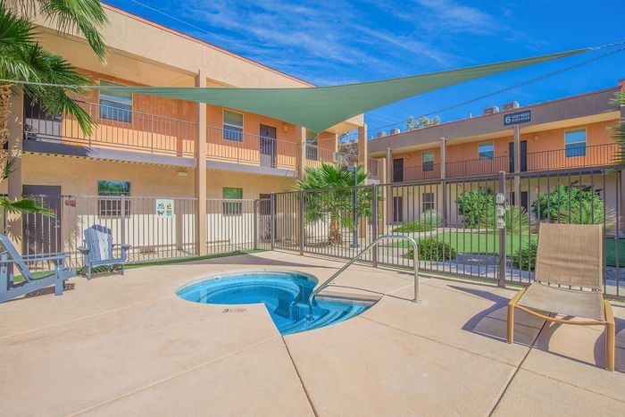 Inviting courtyard featuring a relaxing hot tub shaded by a modern sail canopy, with cozy apartment balconies and lush landscaping.