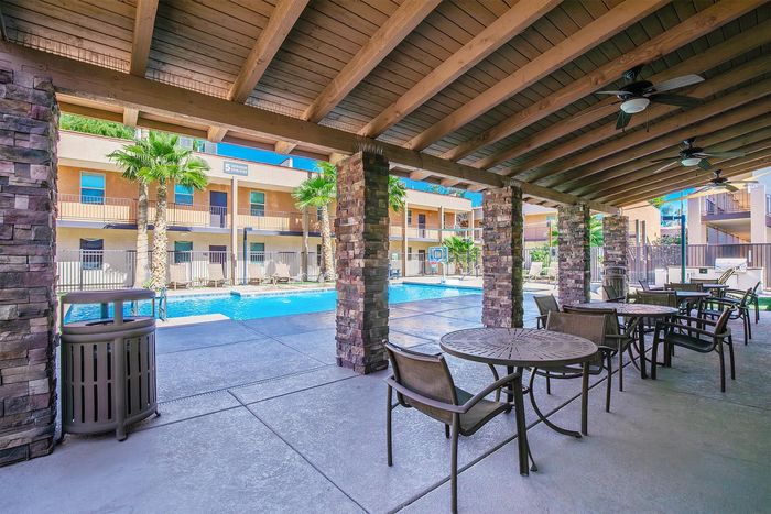 Inviting outdoor space with covered seating overlooking a sparkling pool lined with palm trees in a modern apartment complex.
