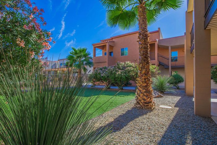 Vibrant courtyard with lush greenery and palm trees in front of modern apartment building under a clear blue sky.