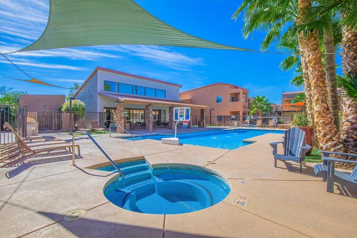 Luxurious apartment complex featuring a sparkling swimming pool, soothing hot tub, and inviting lounging areas under sunny skies.
