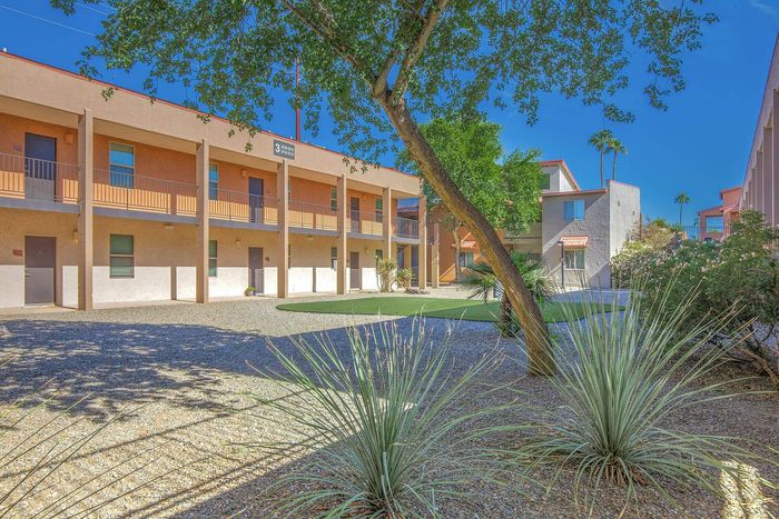 Charming apartment complex with a spacious courtyard, lush greenery, and a sunlit exterior, perfect for a serene living experience.