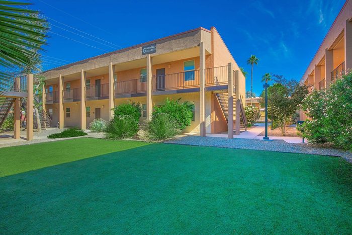 Inviting two-story apartment complex with modern architecture, lush landscaping, and spacious outdoor walkways under a clear blue sky.