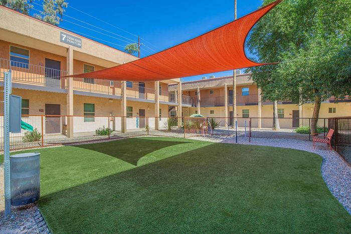 Charming apartment complex courtyard featuring a lush green lawn, modern shade sail, and inviting seating under sunny blue skies.