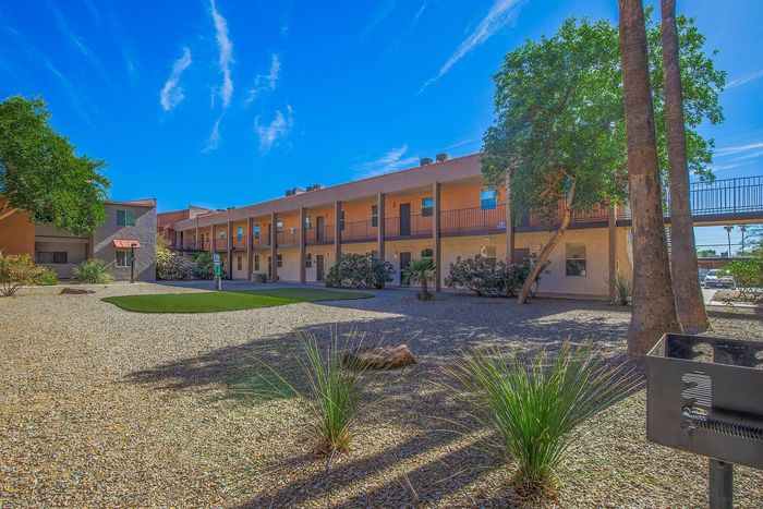 Charming apartment complex with desert landscaping, featuring a two-story building under a vibrant blue sky, perfect for serene living.