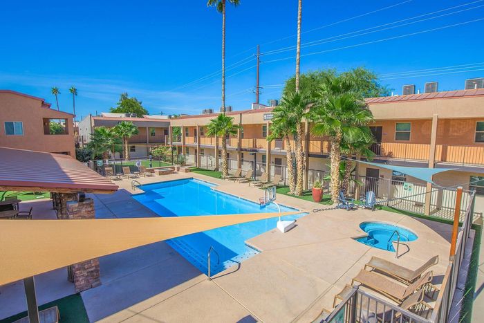 Vibrant apartment complex with a sparkling swimming pool, lush palm trees, and sun-kissed lounging areas, offering a resort-style living experience.