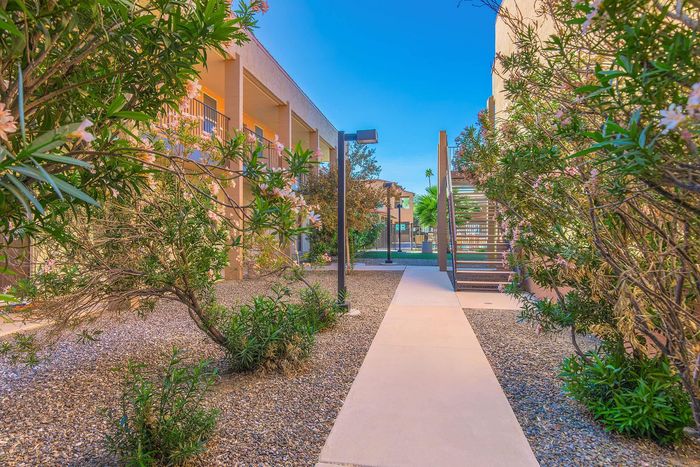Charming landscaped pathway with lush greenery leading to stylish apartment entrances, inviting outdoor space.