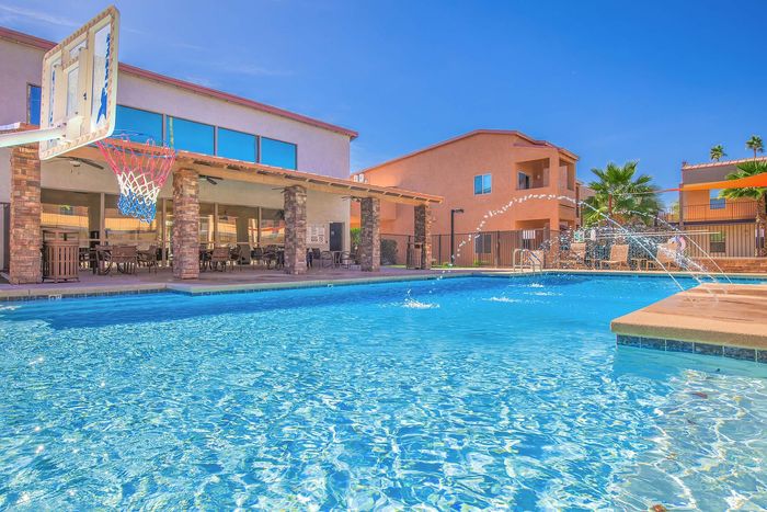 Vibrant apartment community pool with a basketball hoop, elegant seating area, and modern architecture under a clear blue sky.