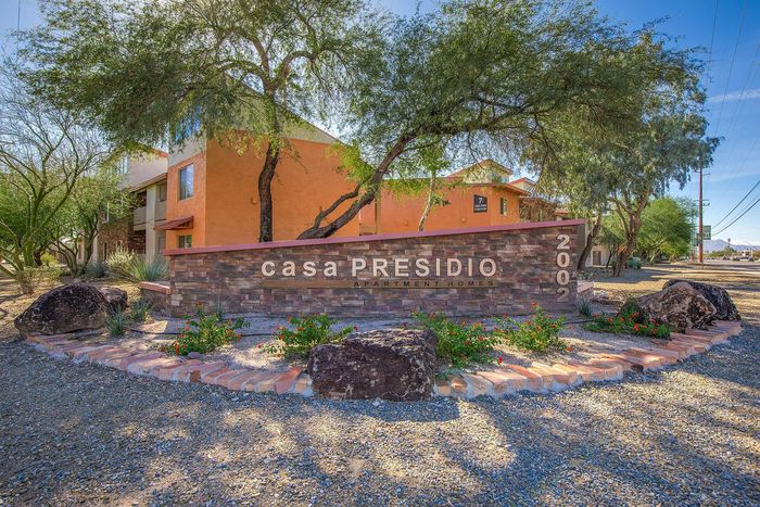 Inviting entrance of Casa Presidio Apartment Homes with lush landscaping and elegant signage under clear blue skies.