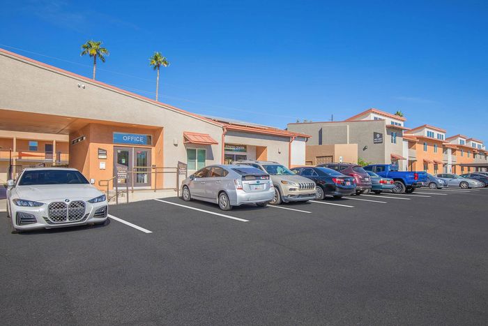 Inviting apartment complex with ample parking under a bright blue sky, featuring a well-maintained office building and fitness center.