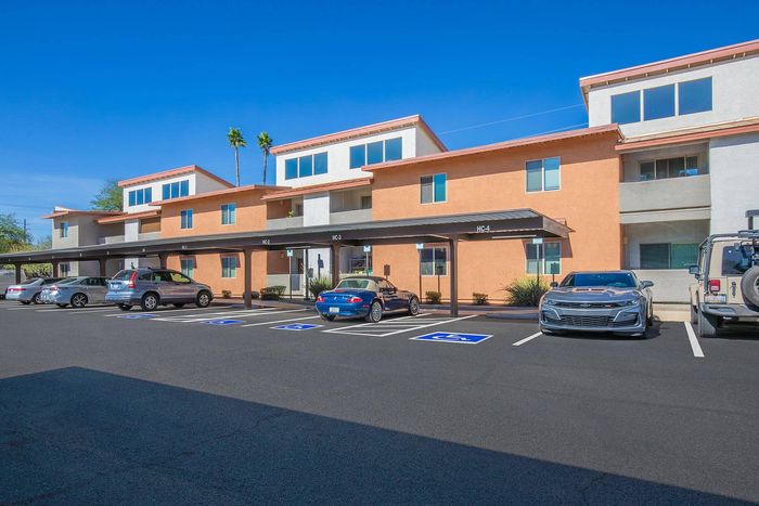 Modern apartment building with covered parking and designated spaces under a clear blue sky.