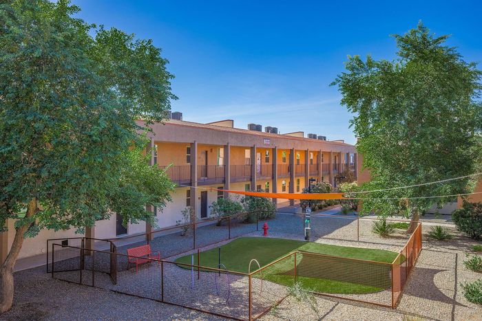 Charming apartment complex with a lush courtyard, vibrant landscape, and inviting outdoor seating area under a clear blue sky.