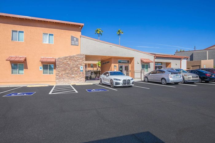 Inviting apartment complex entrance with modern architecture, ample parking, and lush palm trees under a clear blue sky.
