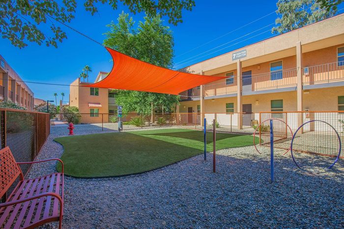 Inviting apartment courtyard featuring a vibrant orange shade sail, lush green lawn, and charming outdoor seating.