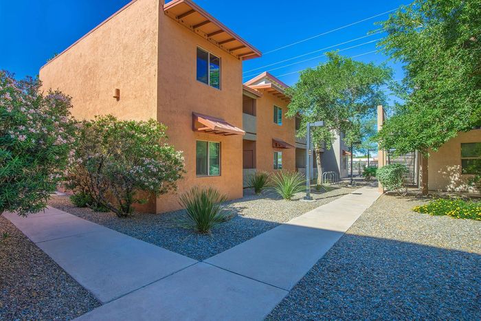 Charming apartment complex with desert landscaping, featuring vibrant stucco buildings and lush greenery under a clear blue sky.