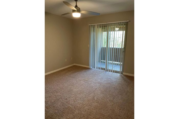 Inviting bedroom with plush carpeting, modern ceiling fan, and sliding glass doors leading to a serene balcony.
