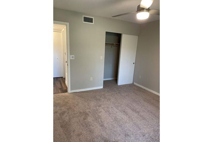 Bright and cozy bedroom with plush carpet, spacious closet with sliding door, and elegant ceiling fan in a modern apartment.