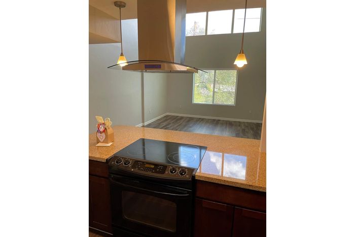 Modern open-concept kitchen with stylish pendant lighting, sleek glass cooktop, and view into a bright, spacious living area with large windows.