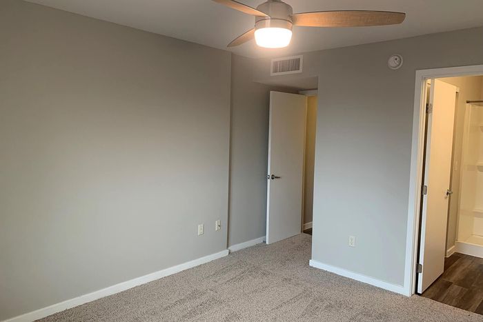 Bright and spacious bedroom featuring soft carpet flooring, modern ceiling fan, and neutral wall tones leading to an en-suite bathroom for ultimate convenience.