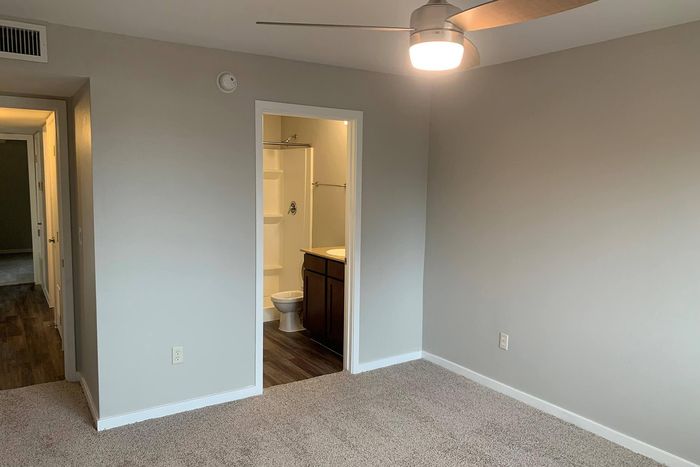 Inviting apartment bedroom with soft carpet flooring and private ensuite bathroom, featuring bright lighting and modern fan for comfort.