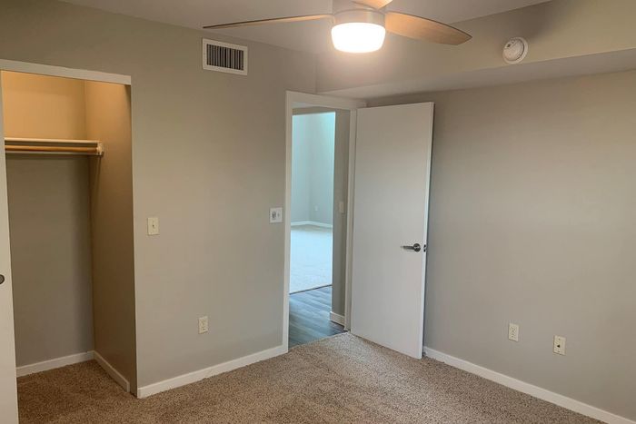 Inviting bedroom with plush carpet, modern ceiling fan, and convenient open closet.