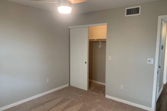 Inviting bedroom with neutral tones, featuring a cozy carpet, illuminated by a stylish ceiling fan and offering a spacious closet with sliding doors.