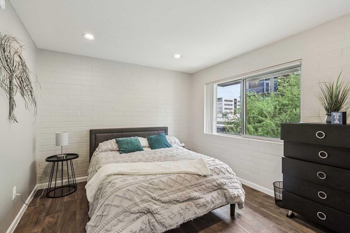 Bright and inviting bedroom with a cozy bed, stylish pillows, modern nightstand, and chic dresser, featuring park views from a large window.