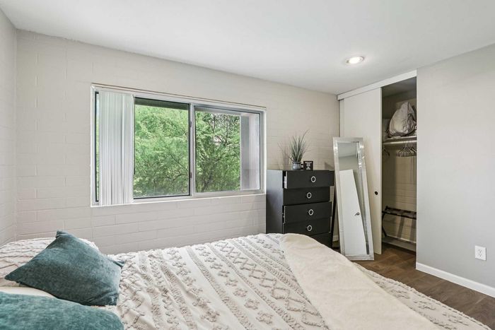Cozy bedroom with large window offering lush green views, featuring a comfortable bed with plush pillows, a sleek black dresser, and a spacious closet.