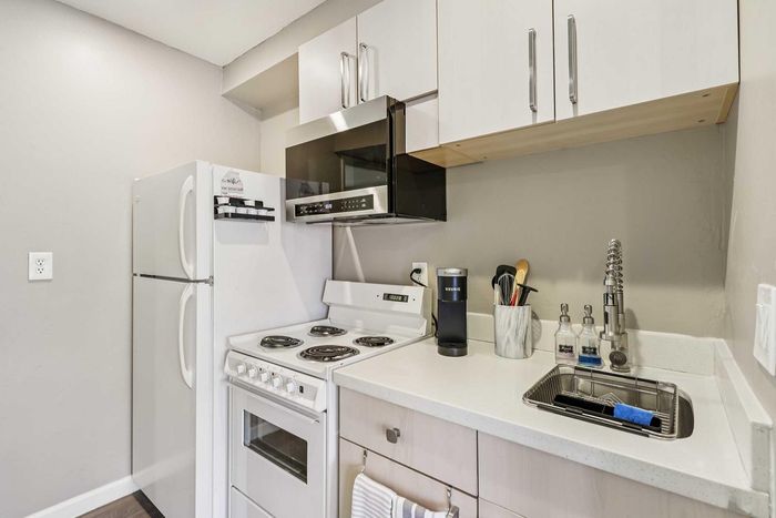 Modern compact kitchen with sleek white cabinets, stainless steel appliances, and stylish countertop, perfect for urban living.